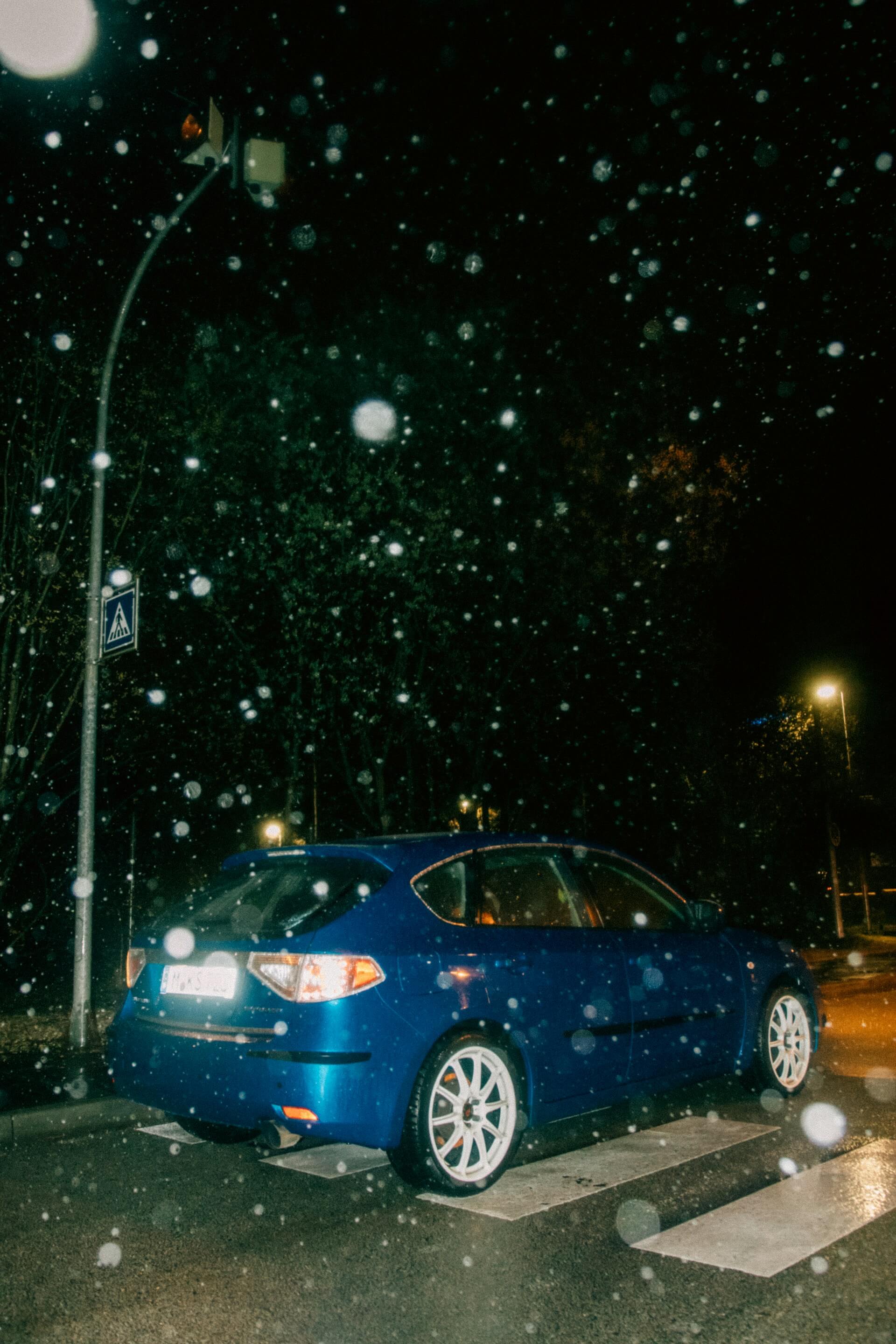 Blue sedan parked along a suburban road during a hailstorm